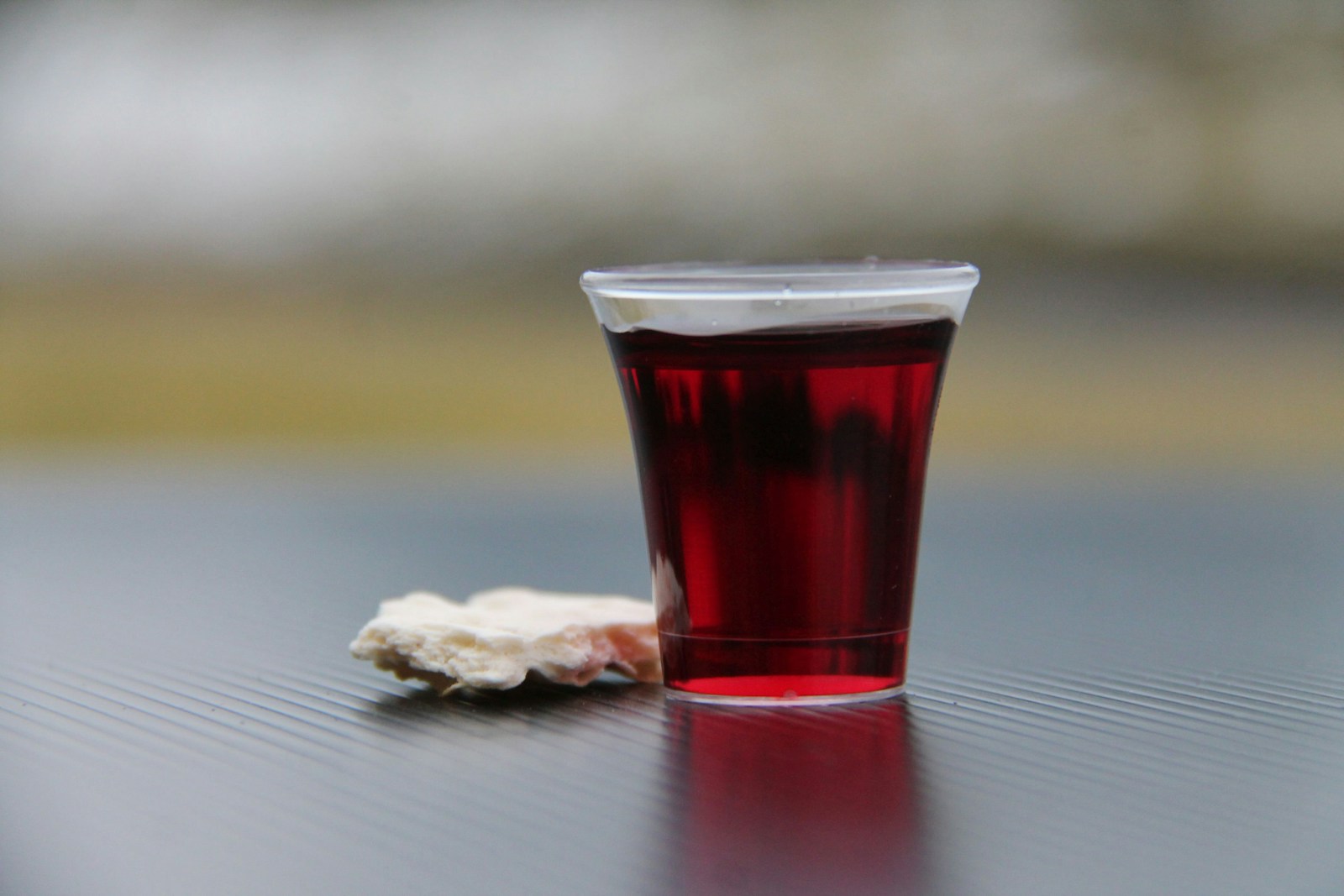 A small cup of red communion wine and a piece of bread on a dark surface