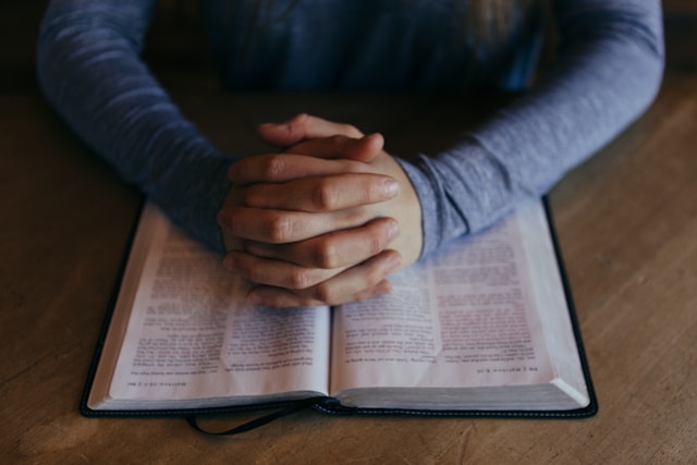 Hands clasped in prayer over an open Bible on a wooden table